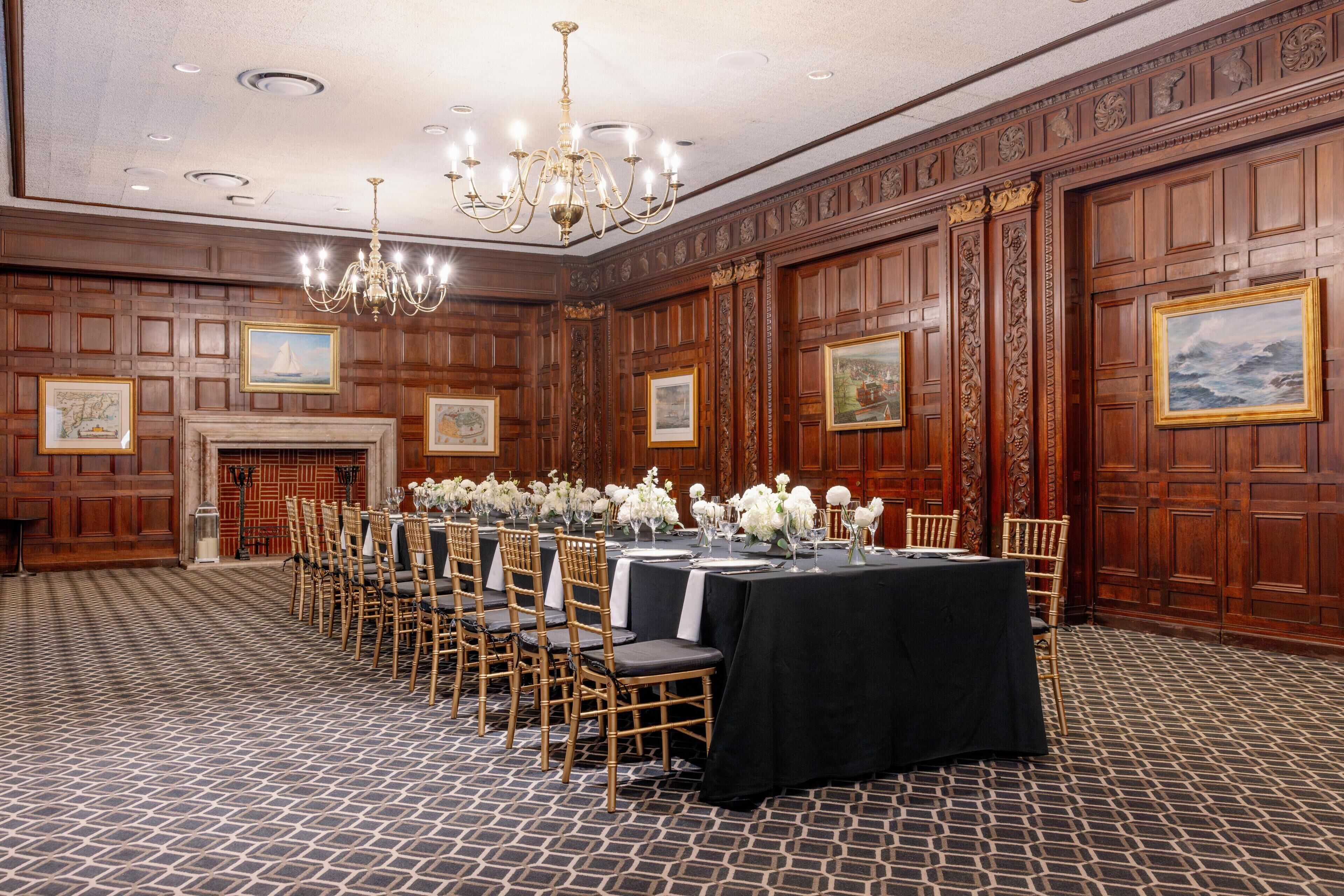 A banquet hall with wooden paneled walls, a chandelier, and a long table set for a formal event.