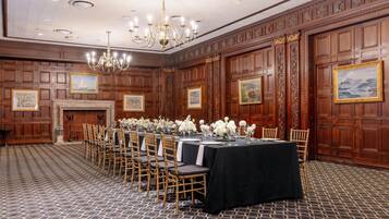 A banquet hall with wooden paneled walls, a chandelier, and a long table set for a formal event.
