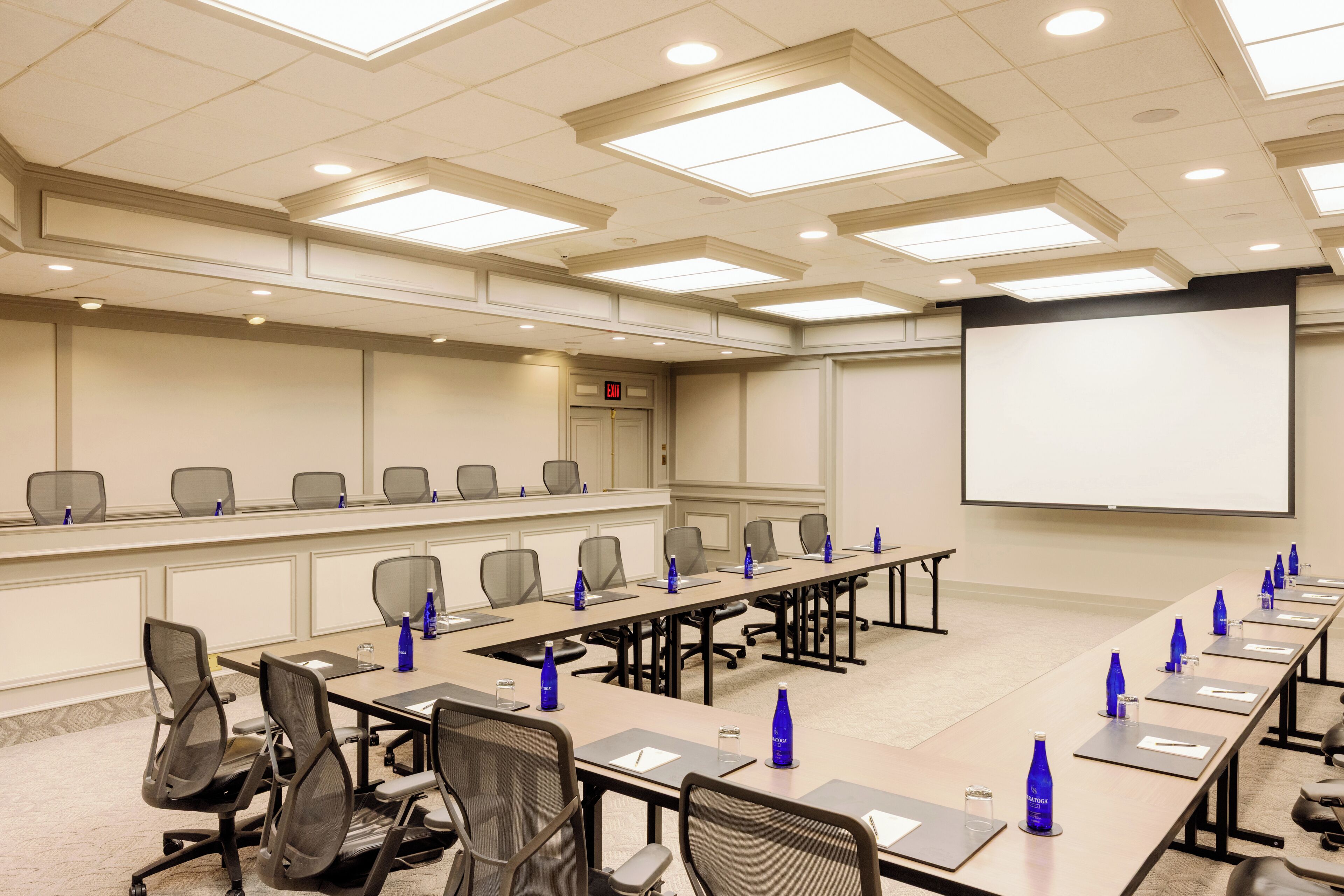 A conference room with a long table, chairs, a projector screen, and a whiteboard.