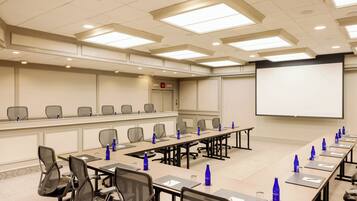 A conference room with a long table, chairs, a projector screen, and a whiteboard.