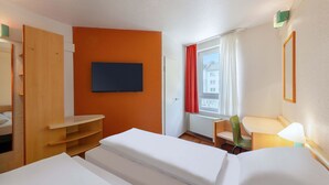 A hotel room with a bed, a TV mounted on the wall, a window with curtains, and a chair. - B&B HOTEL Bochum Hbf-Süd (Bochum)