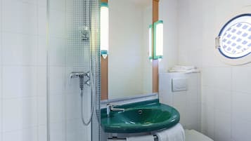 Ein Badezimmer mit Duschkabine aus Glas, einem grünen Waschbecken, einer Toilette und einem beleuchteten Spiegel.
