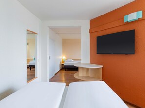 Habitación de hotel con dos camas, un televisor montado en la pared y una mesita pequeña.