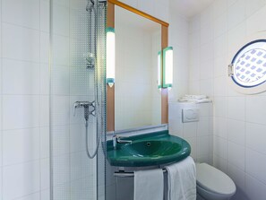 Une salle de bain avec une douche à parois de verre, un lavabo vert, des toilettes et un miroir avec éclairage intégré.