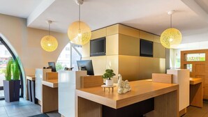 A modern reception desk with two computer monitors, a flat-screen TV, and a decorative elephant sculpture. - B&B HOTEL Bochum Hbf-Süd (Bochum)