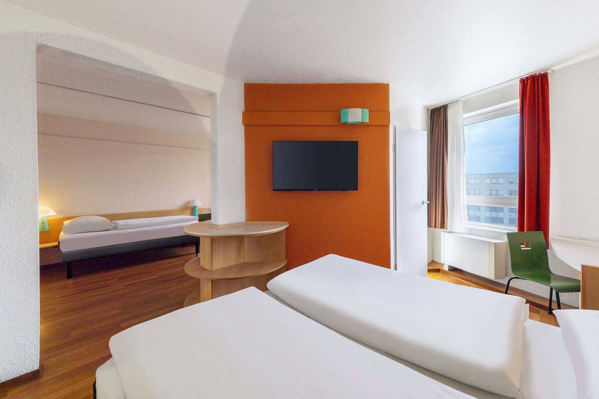 Ein Hotelzimmer mit Bett, Schreibtisch, Stuhl, Fernseher und einem Fenster mit Vorhängen.