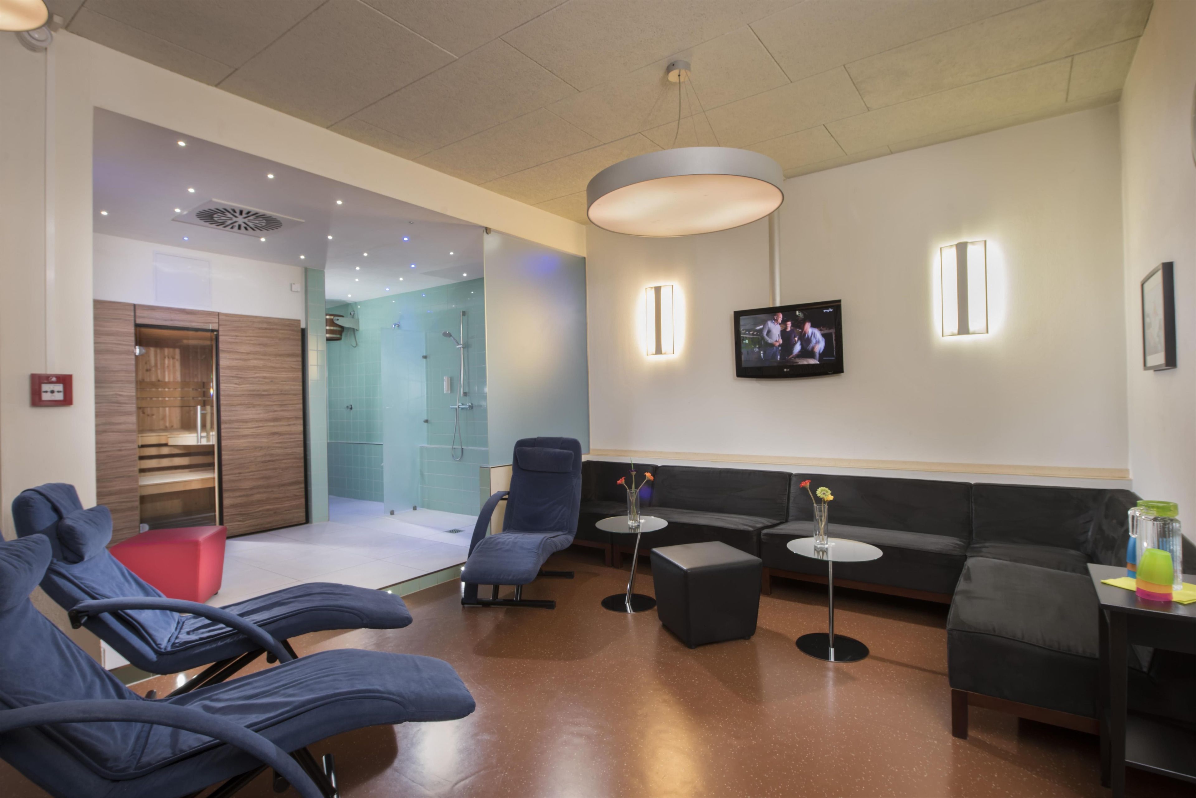 Ett modernt loungeområde med sittplatser, en tv och en duschavdelning med glasväggar.
