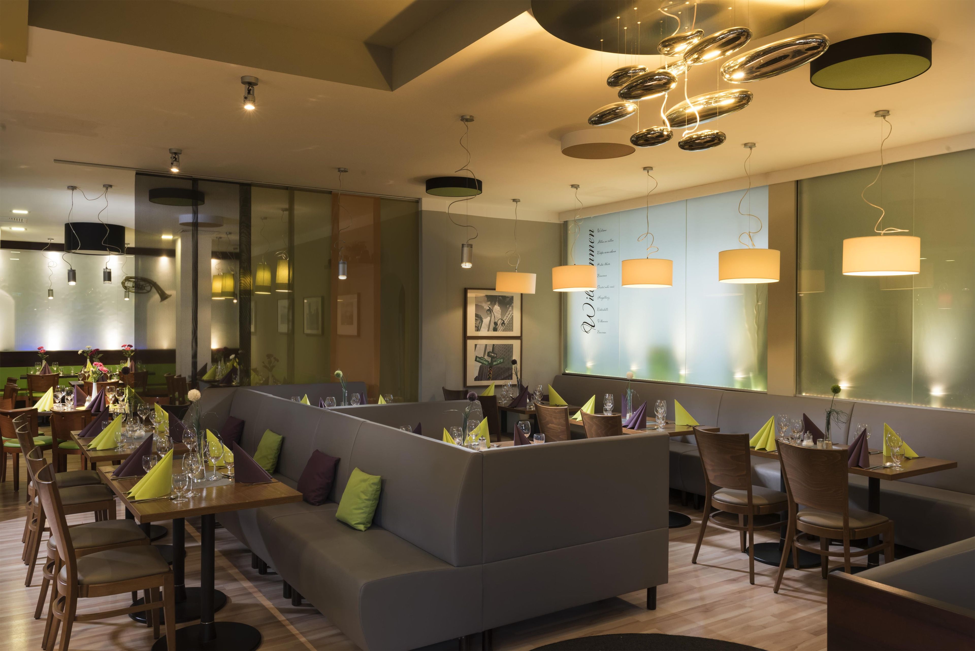 Et moderne restaurantinteriør med et stort fællesskabsbord, polstrede siddepladser og moderne lysarmaturer.
