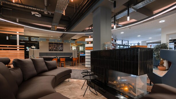 A modern lobby with a sectional sofa, a glass fireplace, and a dining area with wooden tables and chairs. - Best Western Hotel Ambassador (Baunatal)
