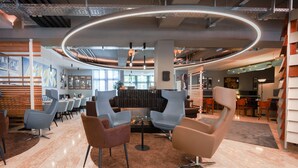 A modern lounge area with contemporary seating, a central fire feature, and a circular light installation on the ceiling. - Best Western Hotel Ambassador (Baunatal)