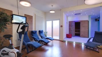 Un área de espera moderna con equipo de ejercicio, asientos y una televisión.