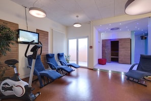 A modern waiting area with exercise equipment, seating, and a television. - Best Western Hotel Ambassador (Baunatal)