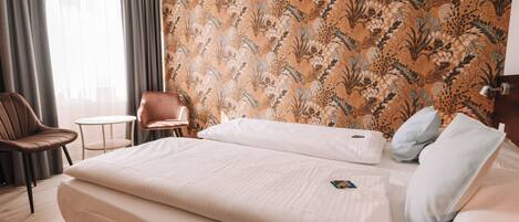 A hotel room with a large bed, a chair, a small table, and a patterned wallpaper.
