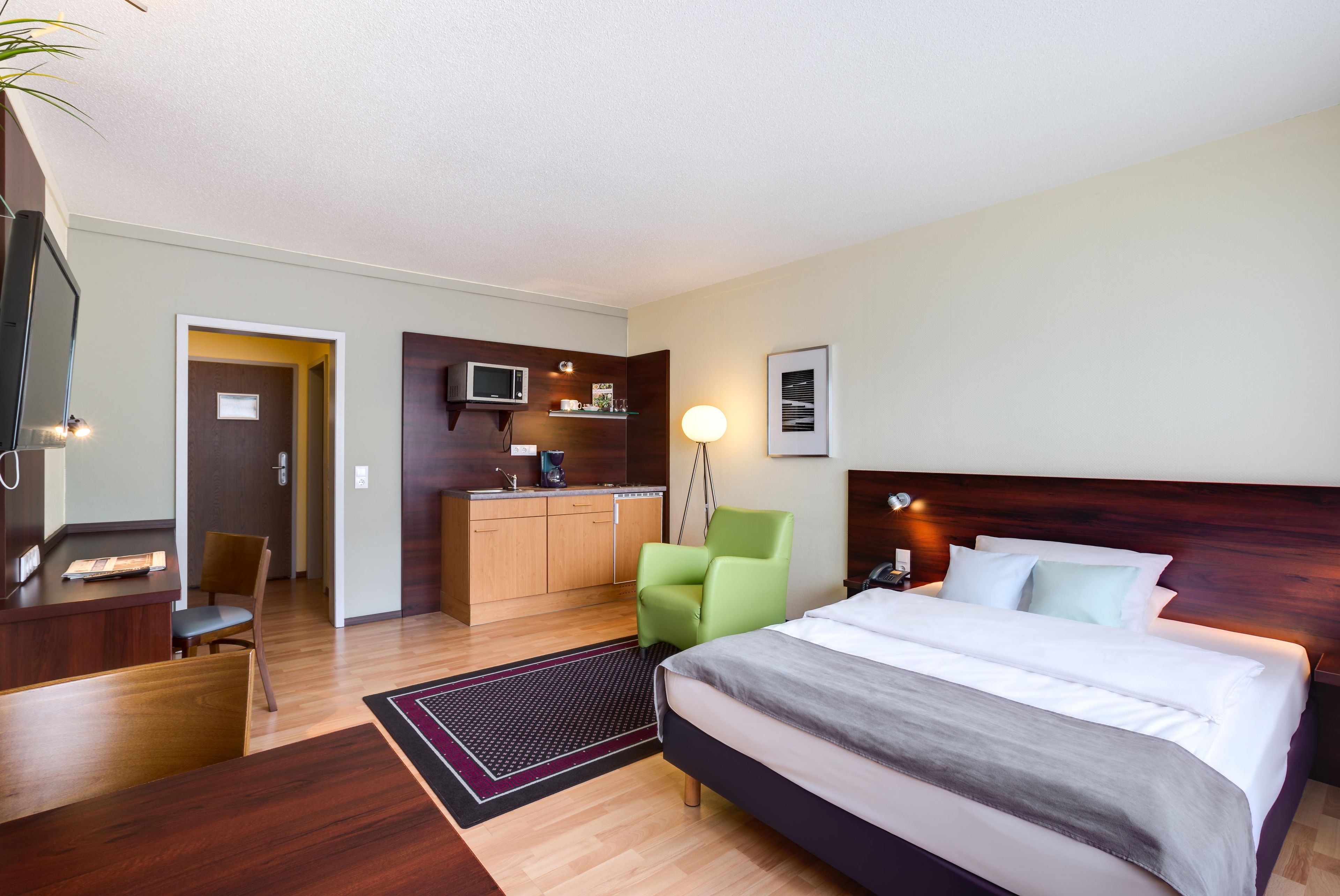 Ein Hotelzimmer mit Bett, Schreibtisch, Stuhl, Küchenzeile und Bad.