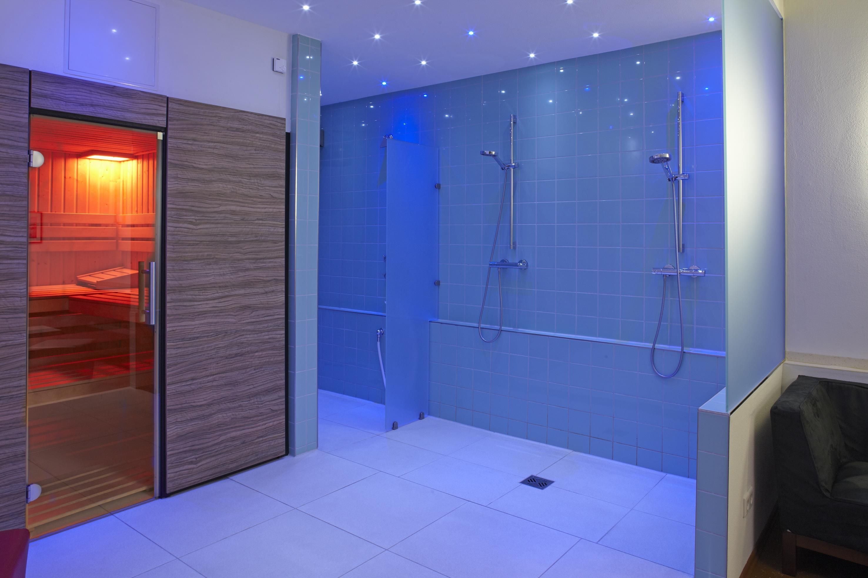 A modern bathroom with a glass shower enclosure, a wooden vanity, and a blue-tiled wall.