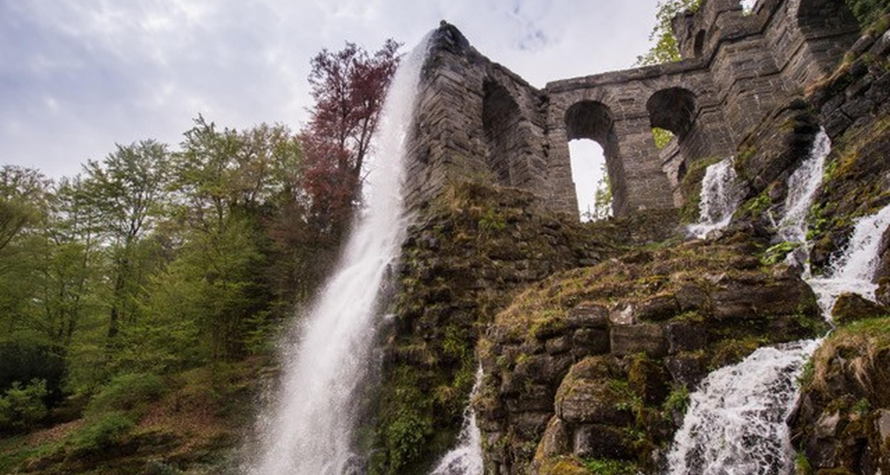 A waterfall cascading down a stone structure with arches, surrounded by trees.