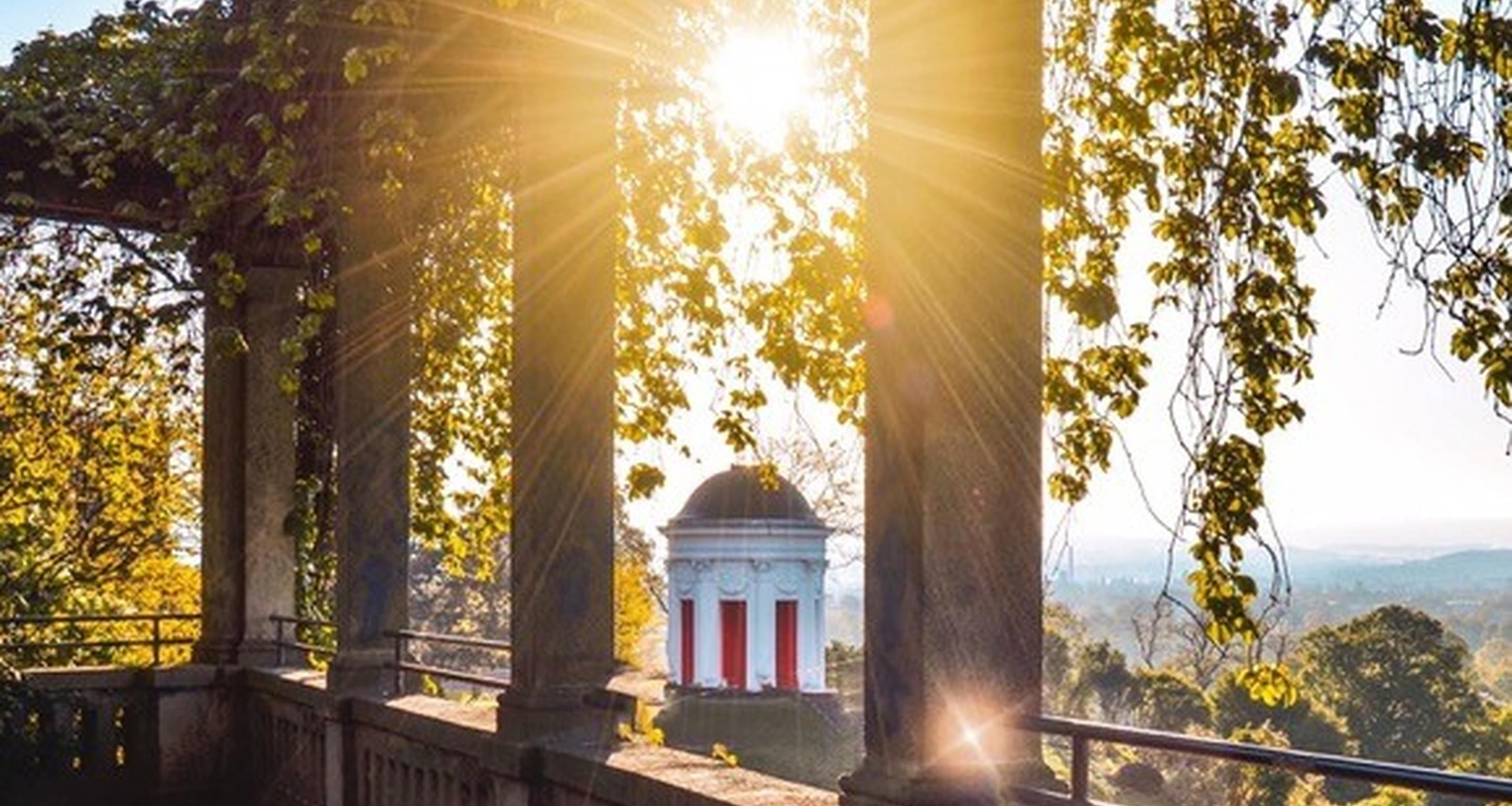 Un bâtiment de style classique, doté de colonnes et d’un dôme, entouré d’arbres et offrant une vue sur le paysage.