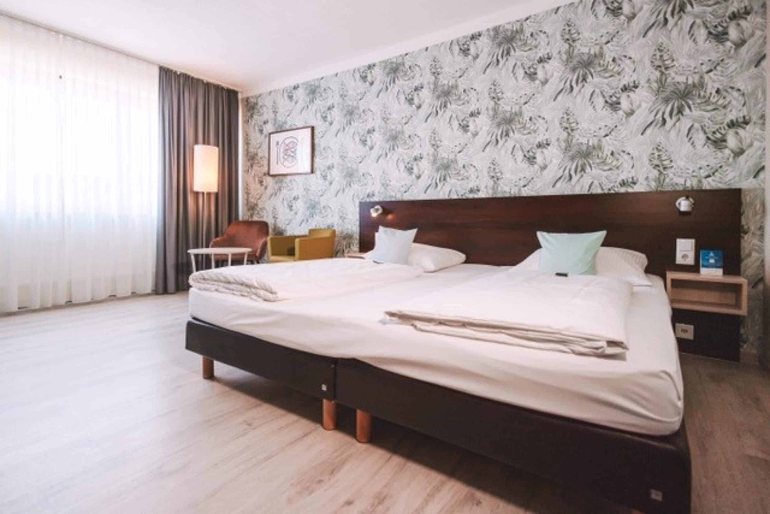 A hotel room with a large bed, a nightstand, a chair, and a window with curtains.
