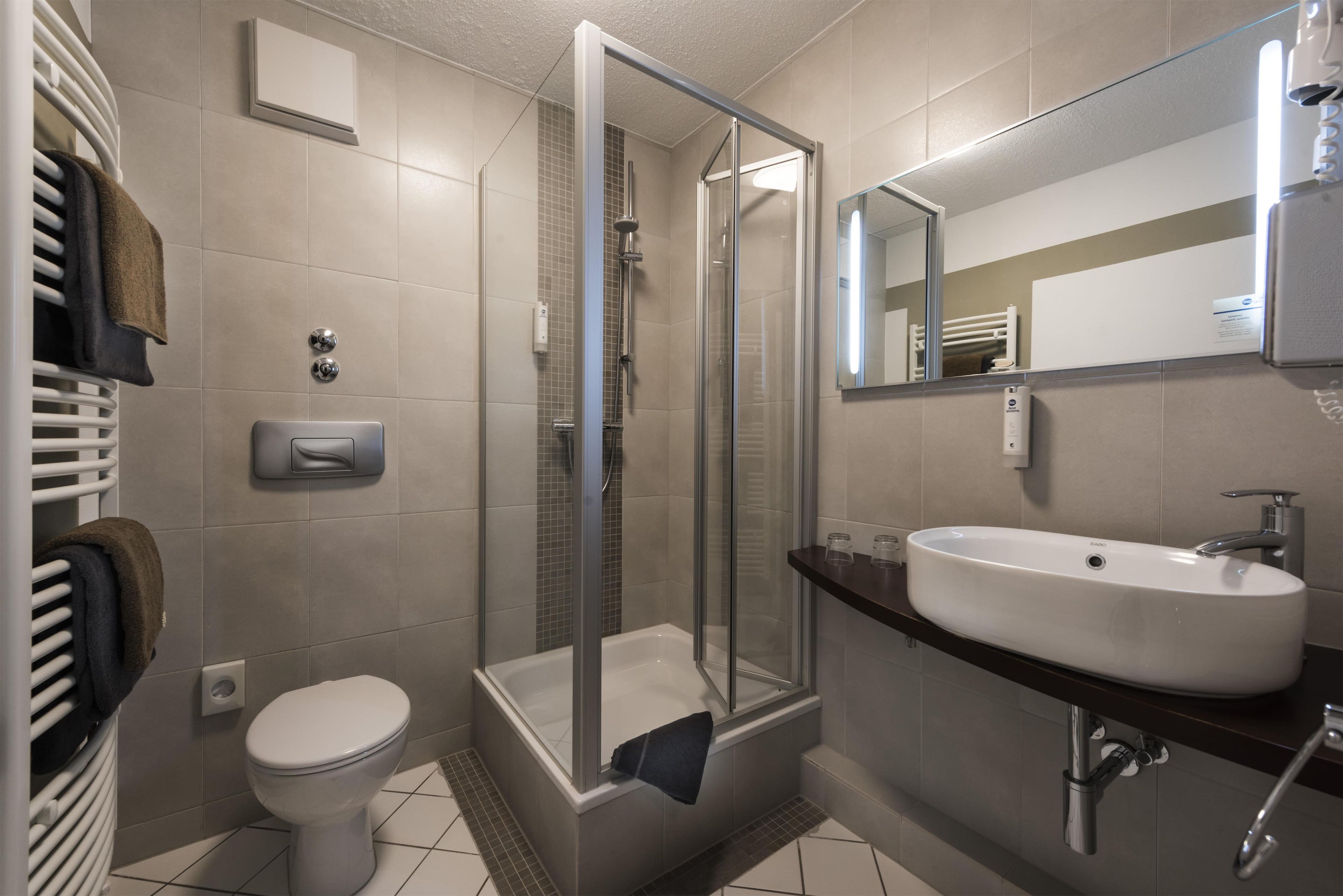 Une salle de bain moderne avec une douche à parois de verre, des toilettes blanches et un grand lavabo surmonté d’un miroir.