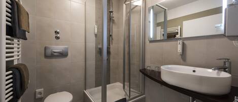 Une salle de bain moderne avec une douche à parois de verre, des toilettes blanches et un grand lavabo surmonté d’un miroir.
