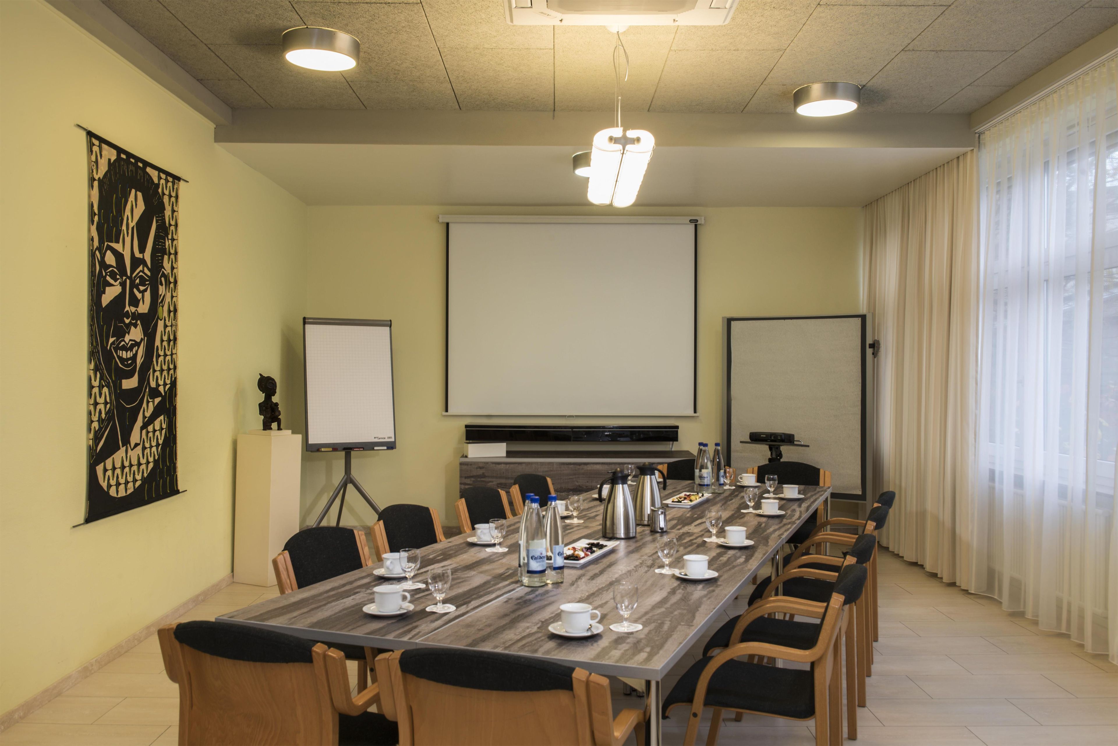 Une salle de conférence équipée d’une longue table, de chaises, d’un écran de projection et d’un tableau blanc.
