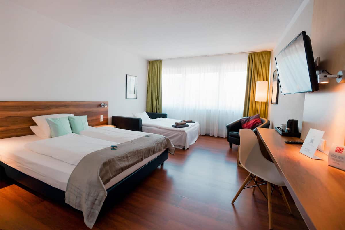 Habitación de hotel con dos camas, un escritorio, una silla, un televisor y una ventana con cortinas.