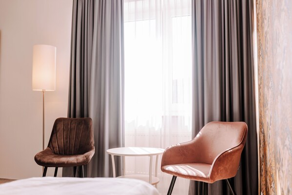 Une chambre d’hôtel avec deux fauteuils en cuir, une petite table ronde et une lampe de chevet.