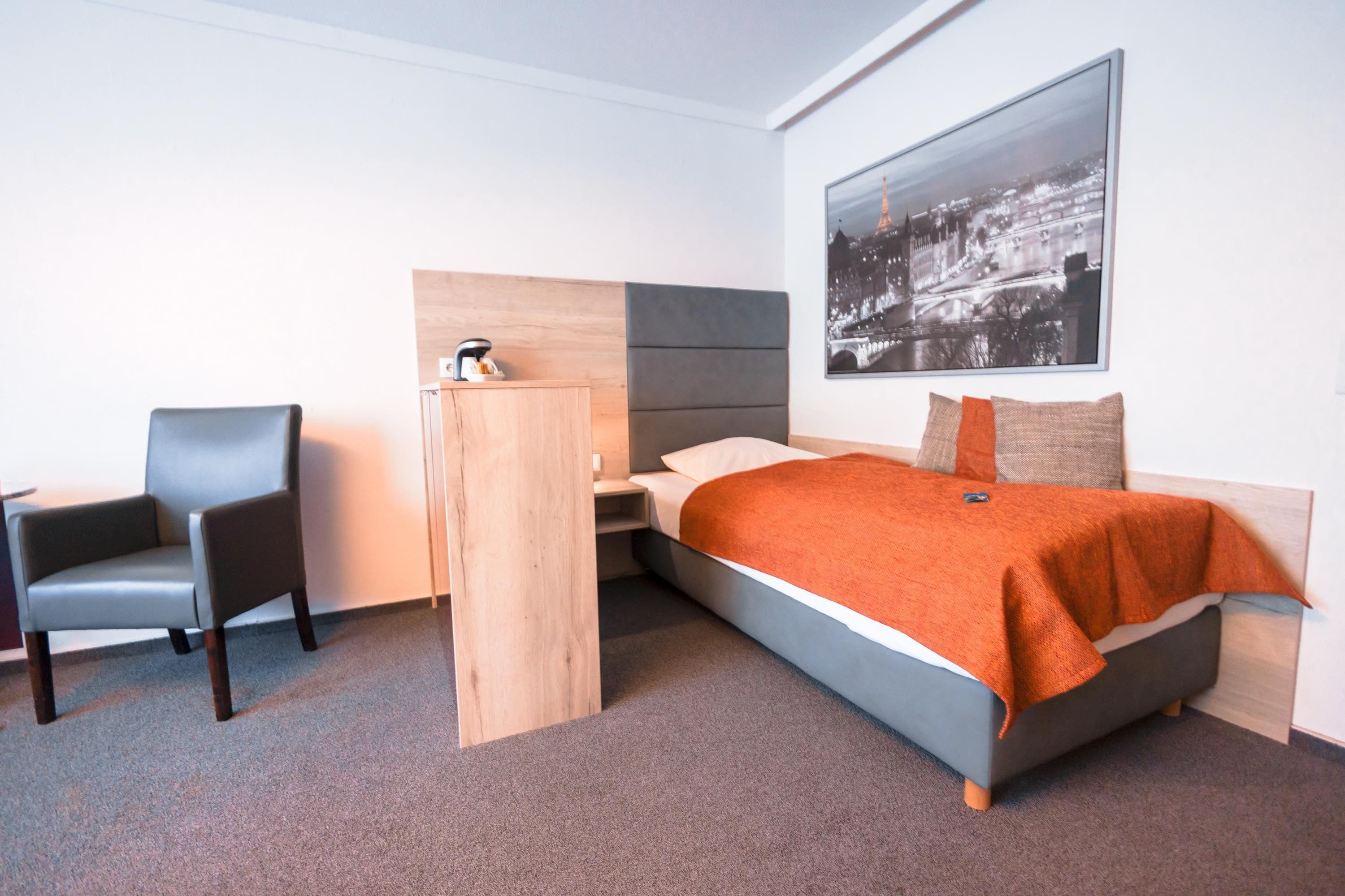 Una habitación de hotel con cama, una silla, una mesita de noche y un cuadro colgado en la pared.