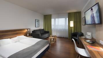 Habitación de hotel con cama, sofá, escritorio con lámpara, silla y televisor.