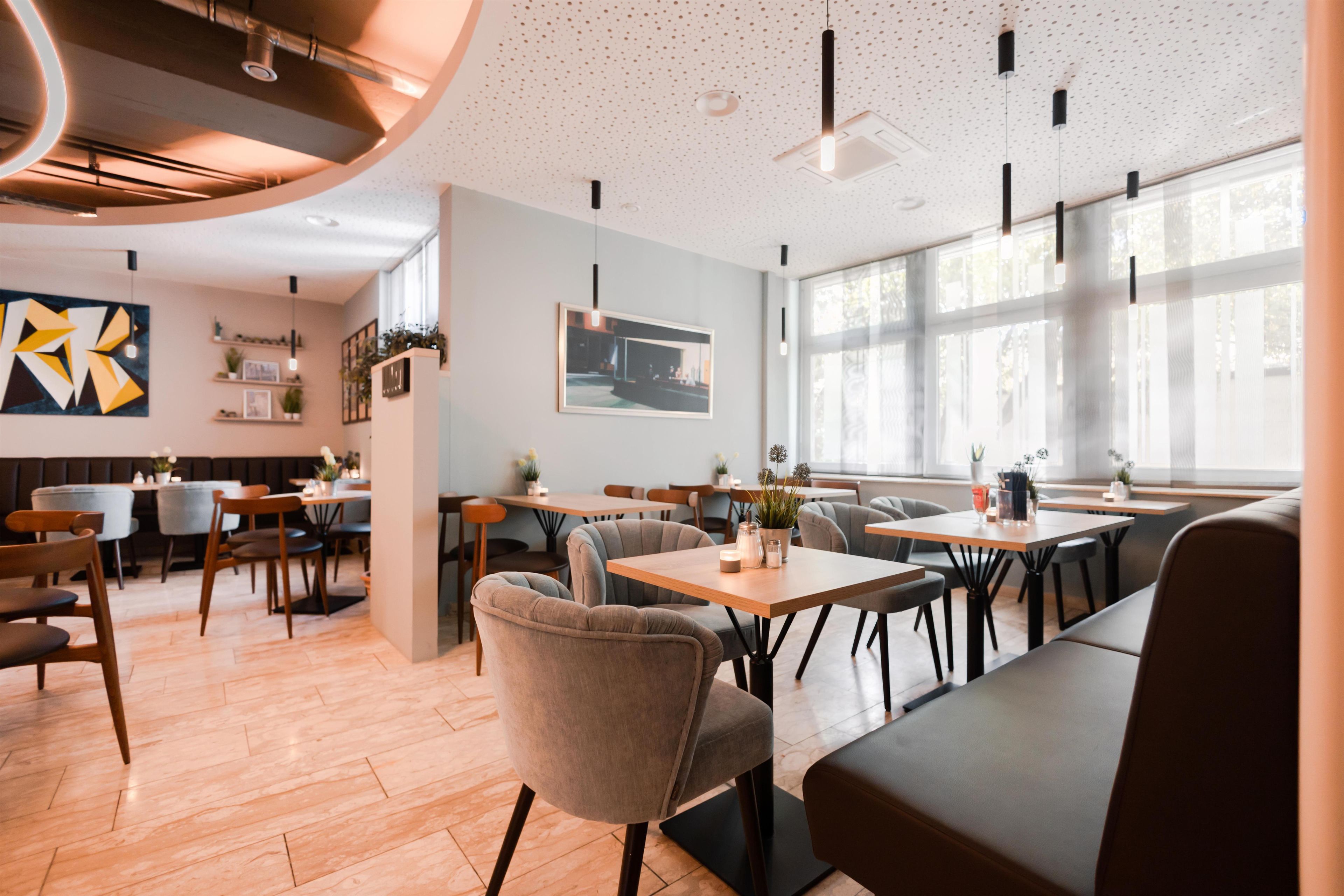 Interior moderno de restaurante con mesas de madera, asientos acolchados e iluminación colgante.