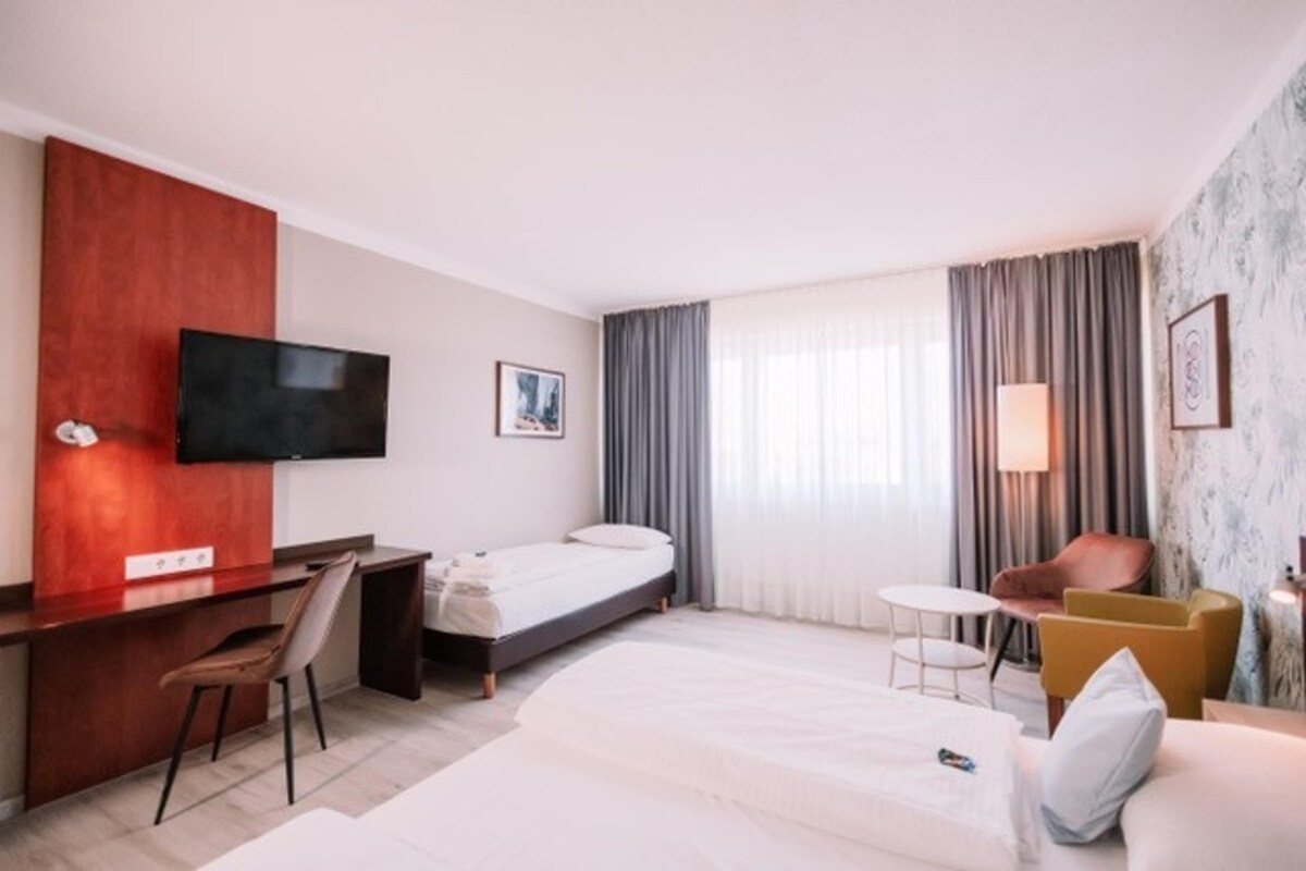 Habitación de hotel con cama, escritorio, silla, televisión, mesita y otra silla.