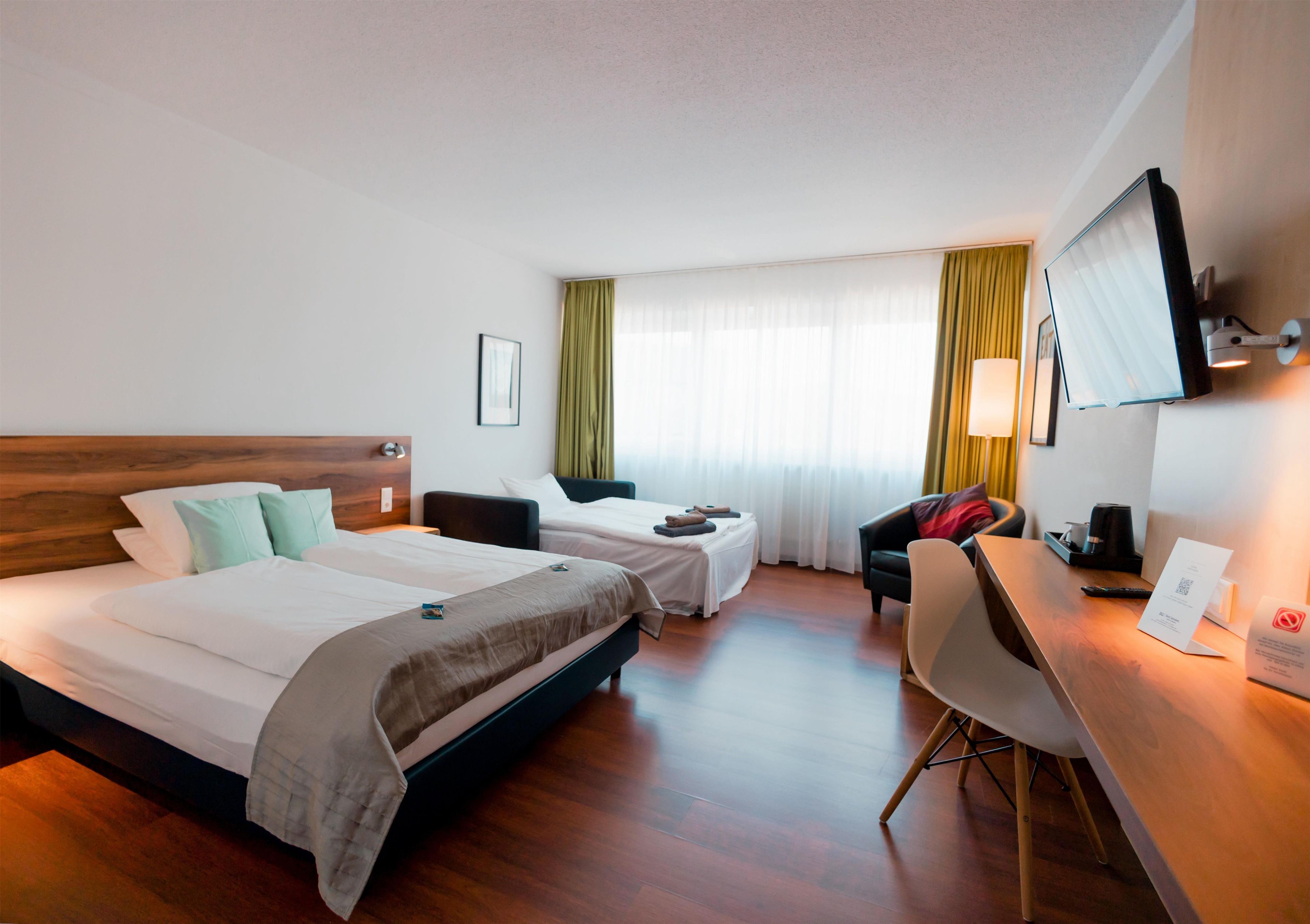 A hotel room with two beds, a desk, a chair, a TV, and a window with curtains.