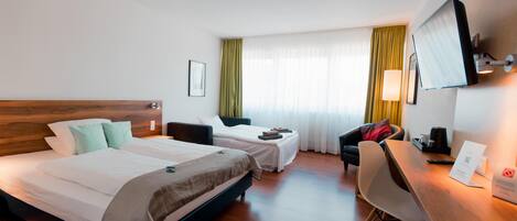 A hotel room with two beds, a desk, a chair, a TV, and a window with curtains.
