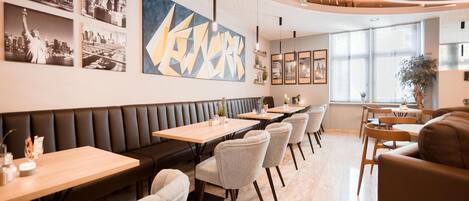A modern restaurant interior with a long counter, cushioned seating, and cityscape artwork on the walls.