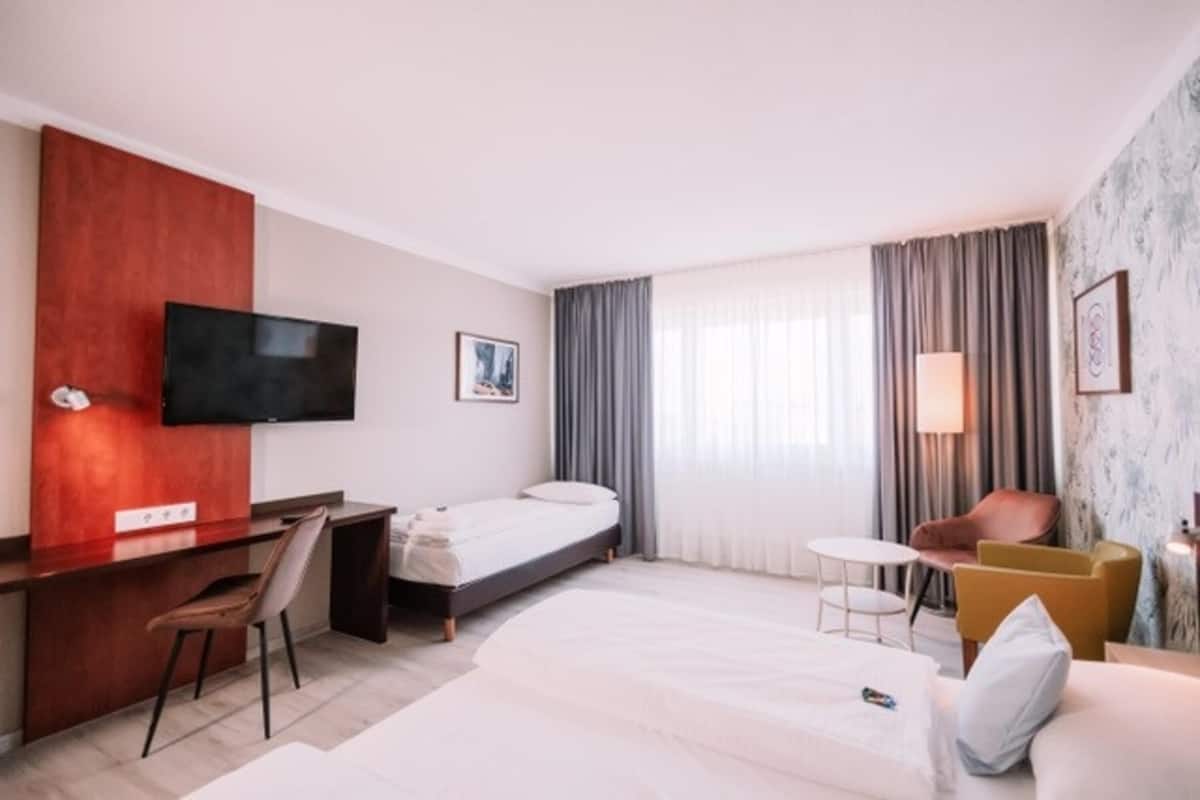 Habitación de hotel con cama, escritorio, silla, televisión, mesita y otra silla.