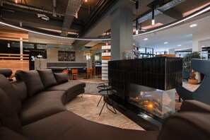 A modern lobby with a sectional sofa, a glass fireplace, and a dining area with wooden tables and chairs. - Best Western Hotel Ambassador (Baunatal)