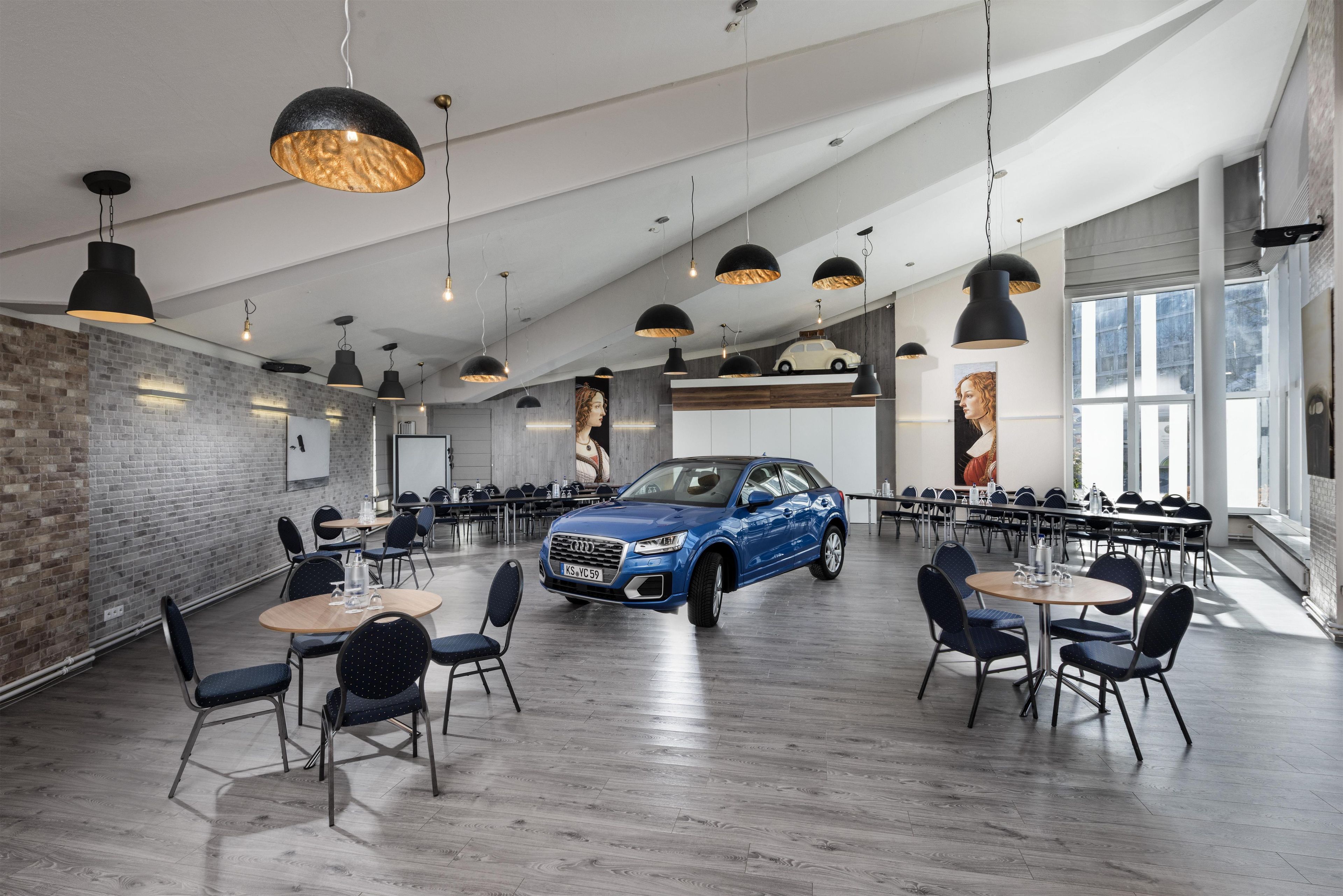 A spacious conference room with modern pendant lighting, a blue car parked inside, and a brick wall.