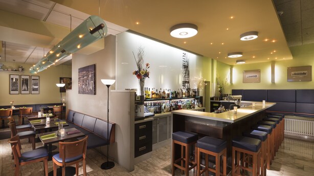 A bar area with a long counter, bar stools, and a seating area with tables and chairs. - Best Western Hotel Ambassador (Baunatal)
