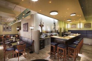 Un espace bar doté d’un long comptoir, de tabourets et d’un coin salon avec des tables et des chaises.
