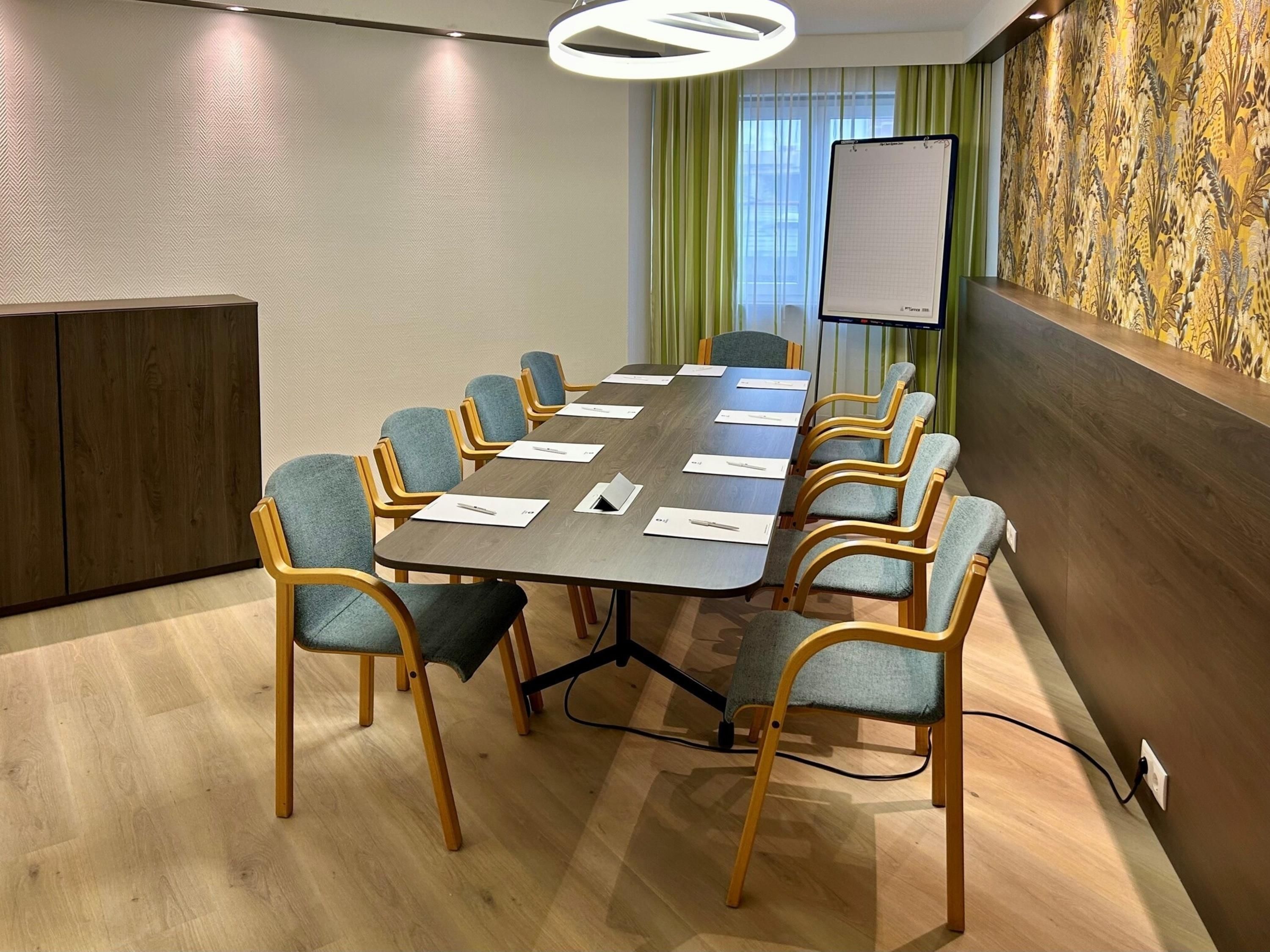 Un salón de conferencias con una larga mesa, seis sillas, una pantalla de proyector y un papel tapiz estampado.