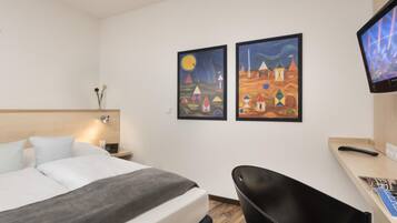 Ein Hotelzimmer mit einem Bett, einem Schreibtisch mit Computer, einem Sessel und zwei Bildern an der Wand.