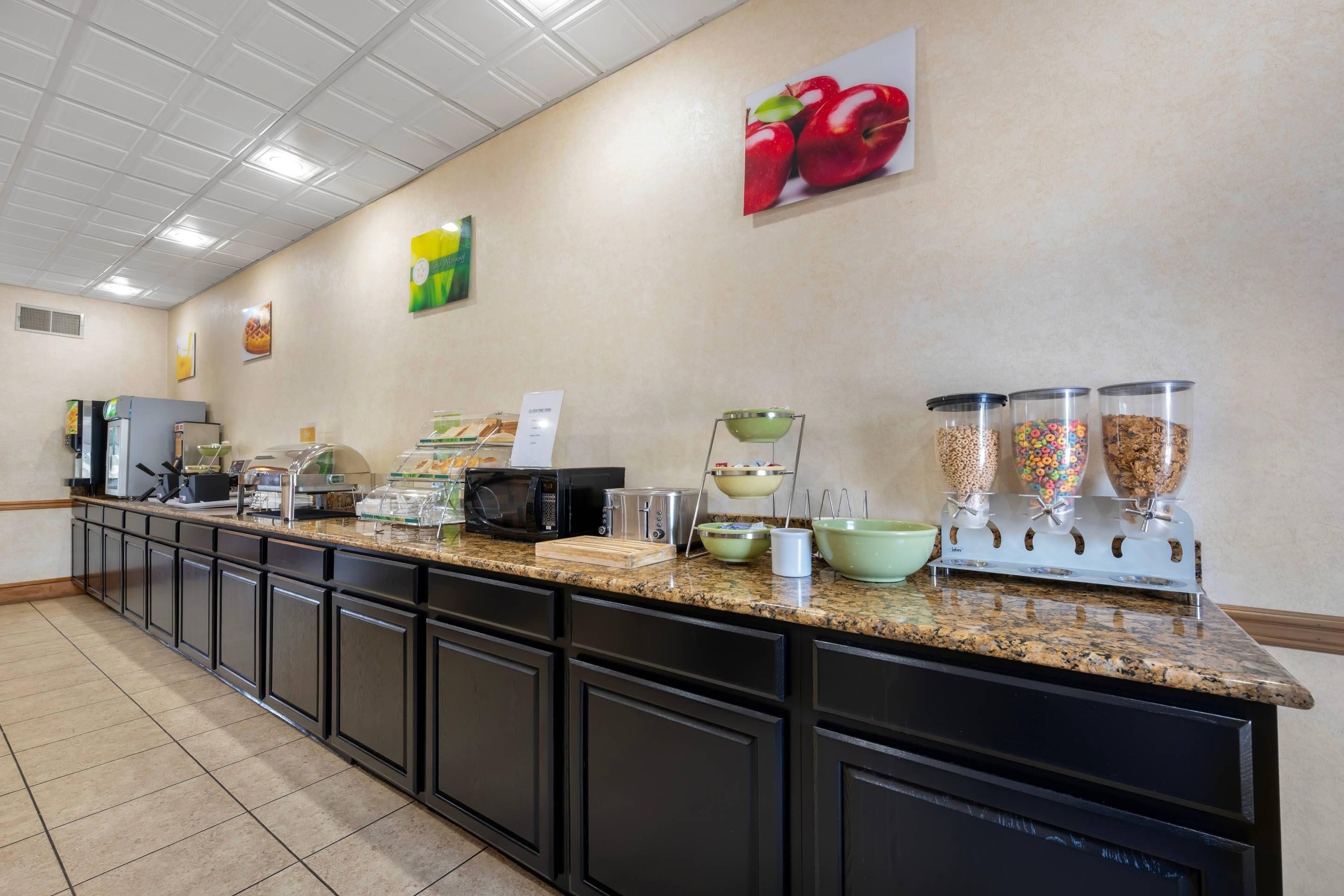 A buffet area with a variety of food items, including cereal and fruits, and a microwave.