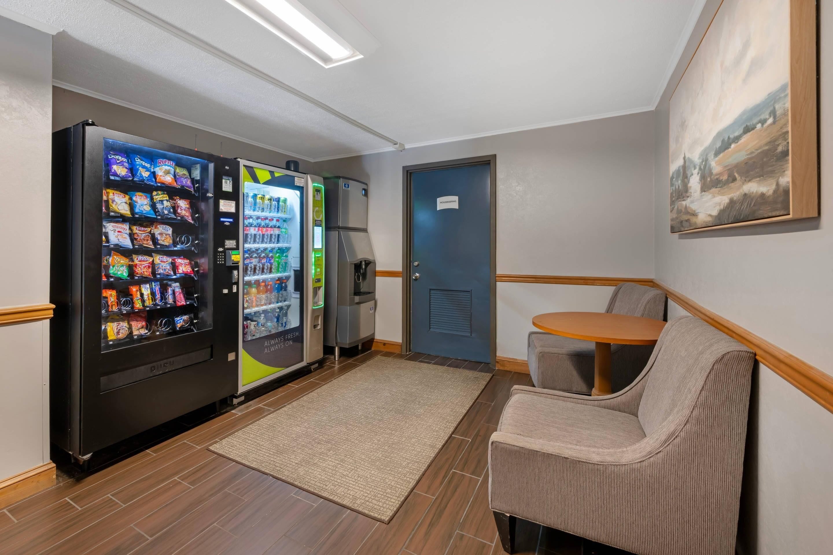 A room with a vending machine, a refrigerator, a microwave, a small table, and a chair.