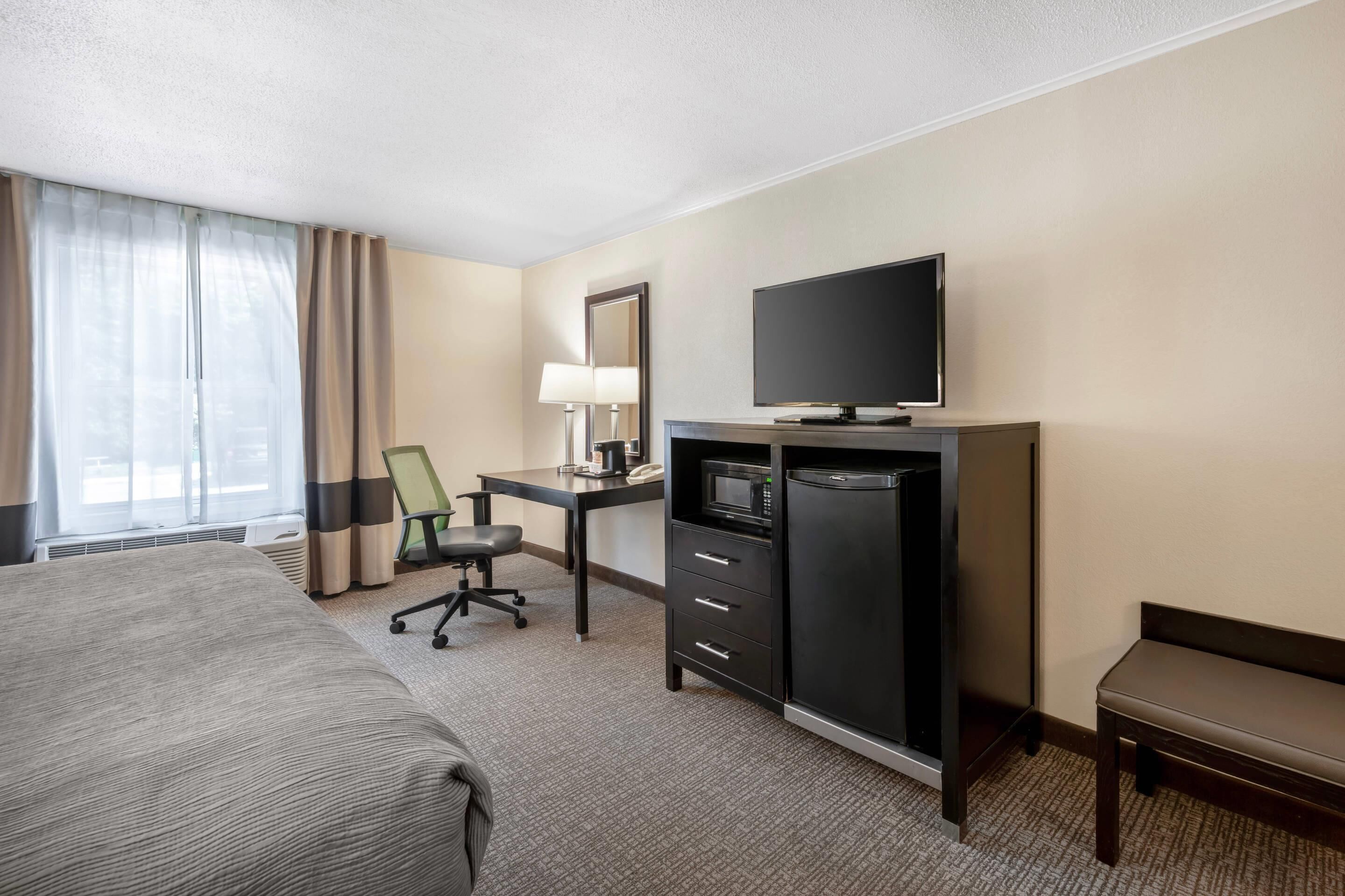 A hotel room with a bed, a desk with a computer, a television, and a minibar.