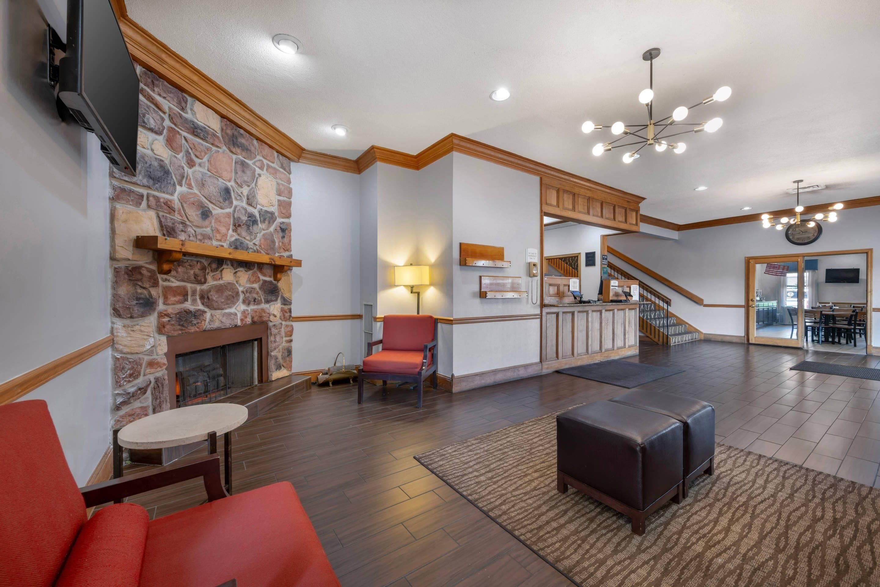 A spacious lobby with a stone fireplace, a red armchair, a modern chandelier, and a staircase leading to a dining area.