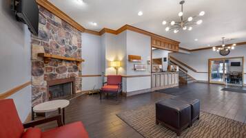 A spacious lobby with a stone fireplace, a red armchair, a modern chandelier, and a staircase leading to a dining area.