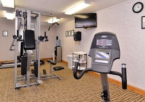 Un gimnasio de hotel con equipo de cardio, un televisor y un reloj en la pared.