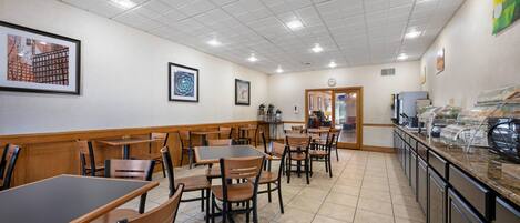 A restaurant with multiple tables and chairs, a kitchen area, and framed artwork on the walls.