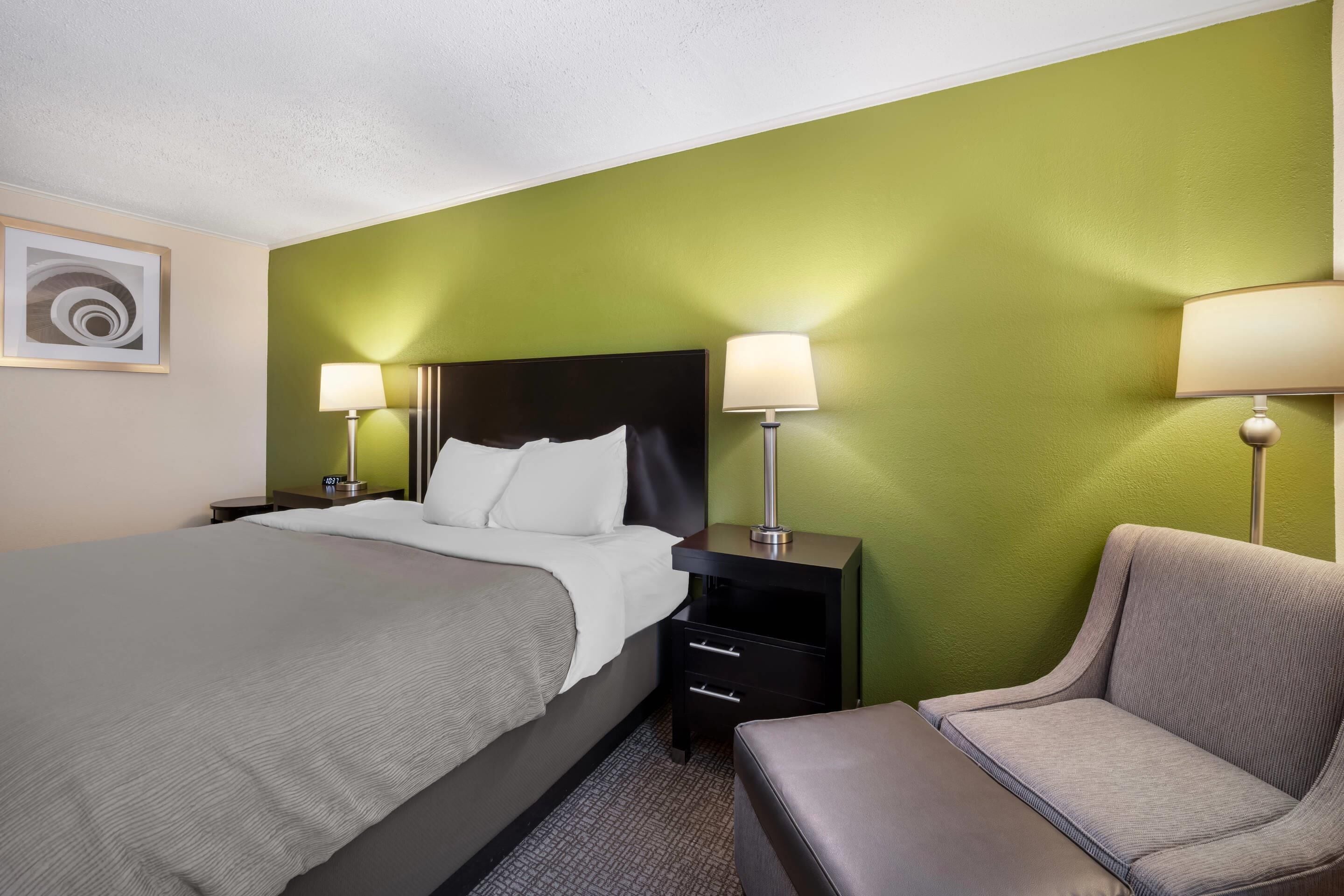 A hotel room with a bed, two bedside tables with lamps, a chair, and a wall art piece.