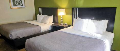 A hotel room with two beds, a nightstand with a lamp, and a framed picture on the wall.